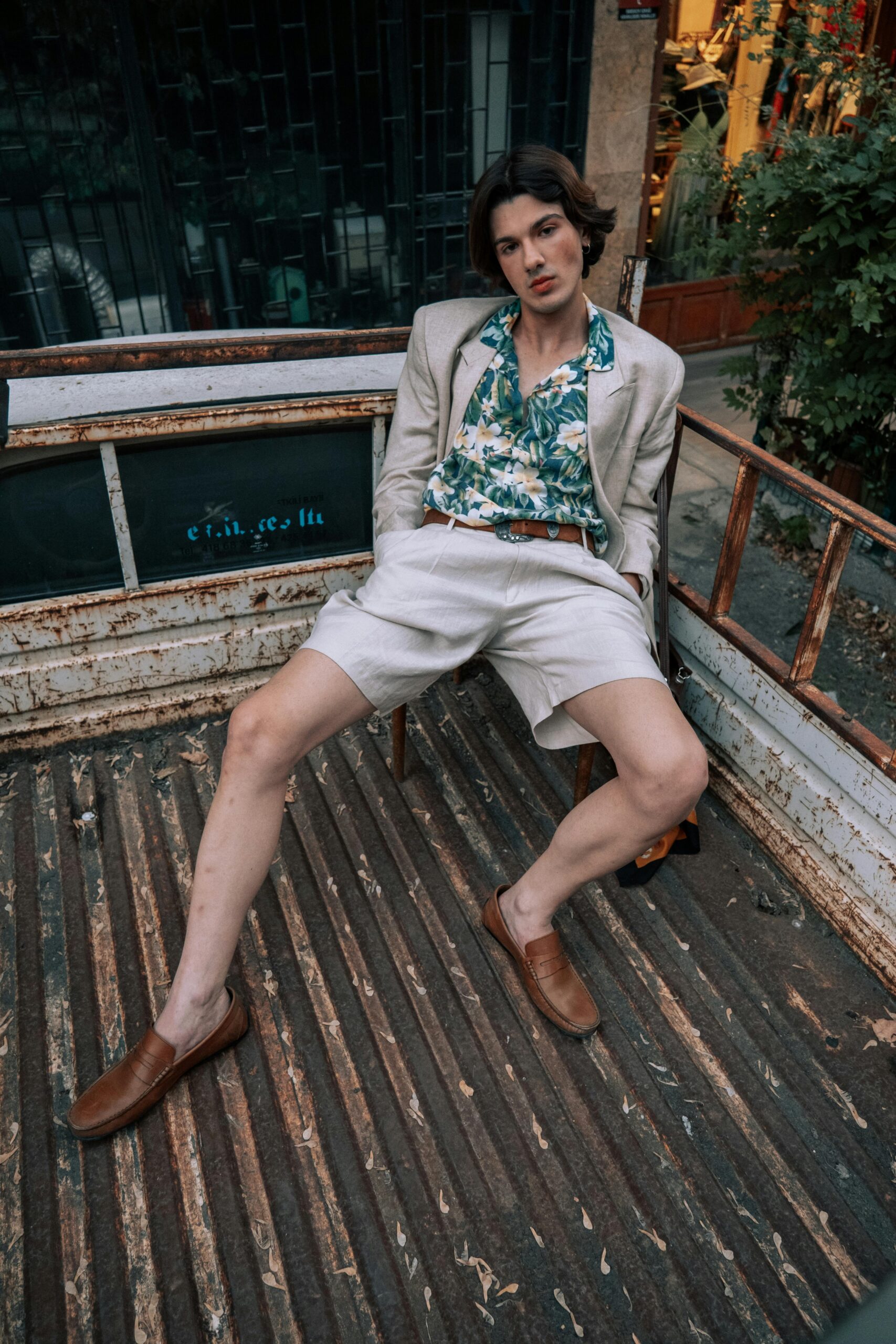 Confident man sitting in a truck bed, showcasing summer fashion with a blazer and floral shirt.