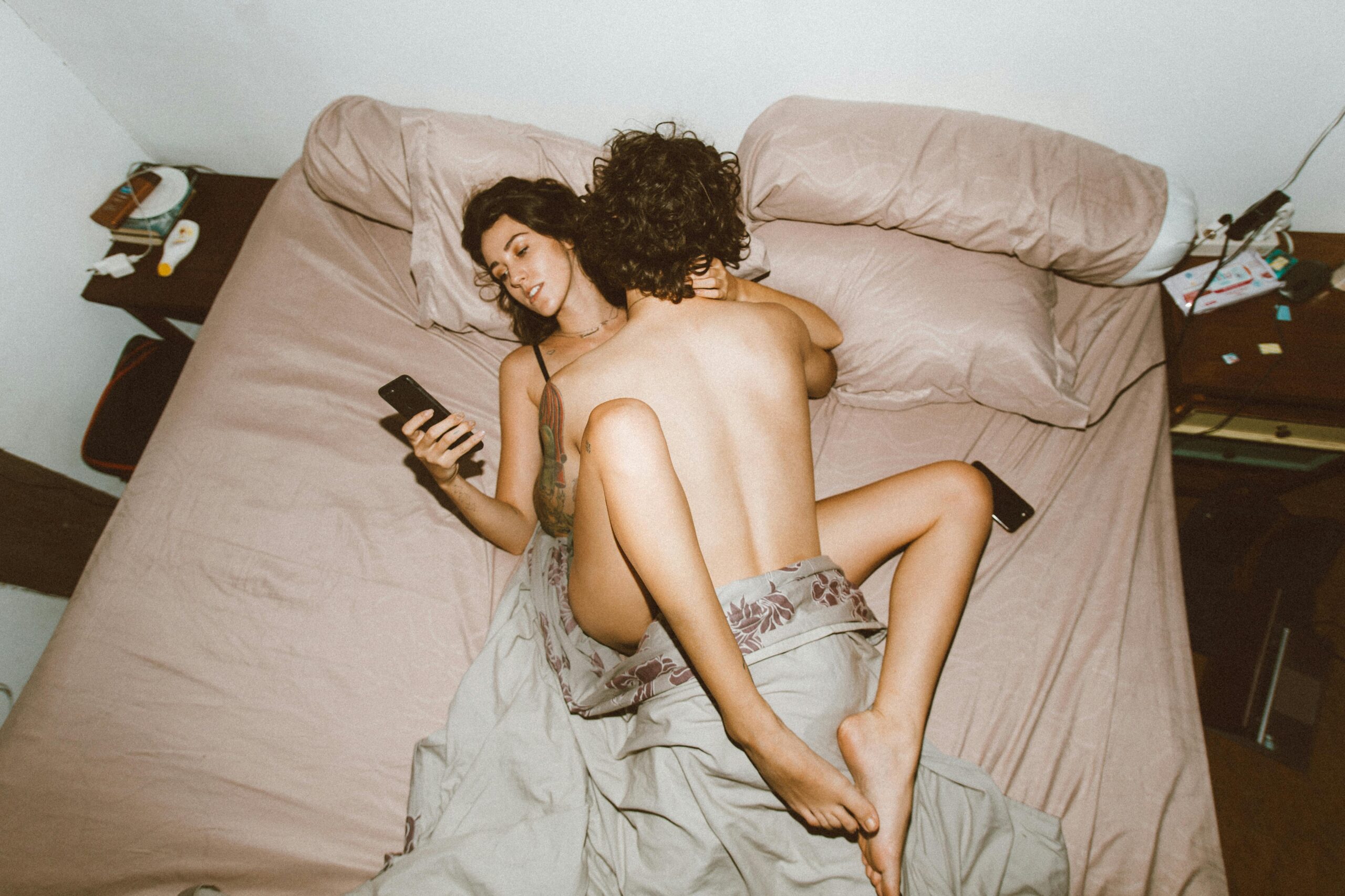 A couple in bed looking at smartphones, highlighting modern disconnection.