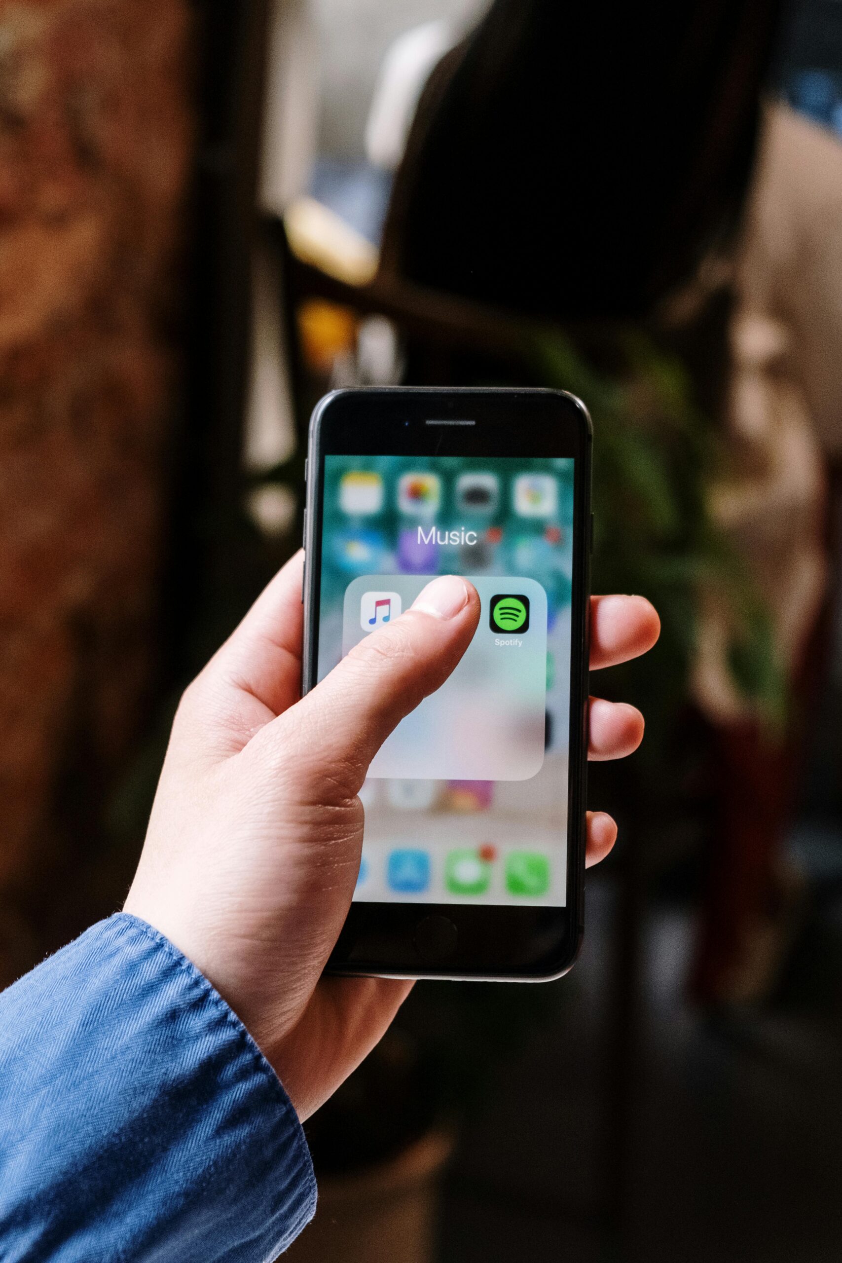 Close-up of a hand holding a smartphone displaying music apps like Spotify and Apple Music, indoors.