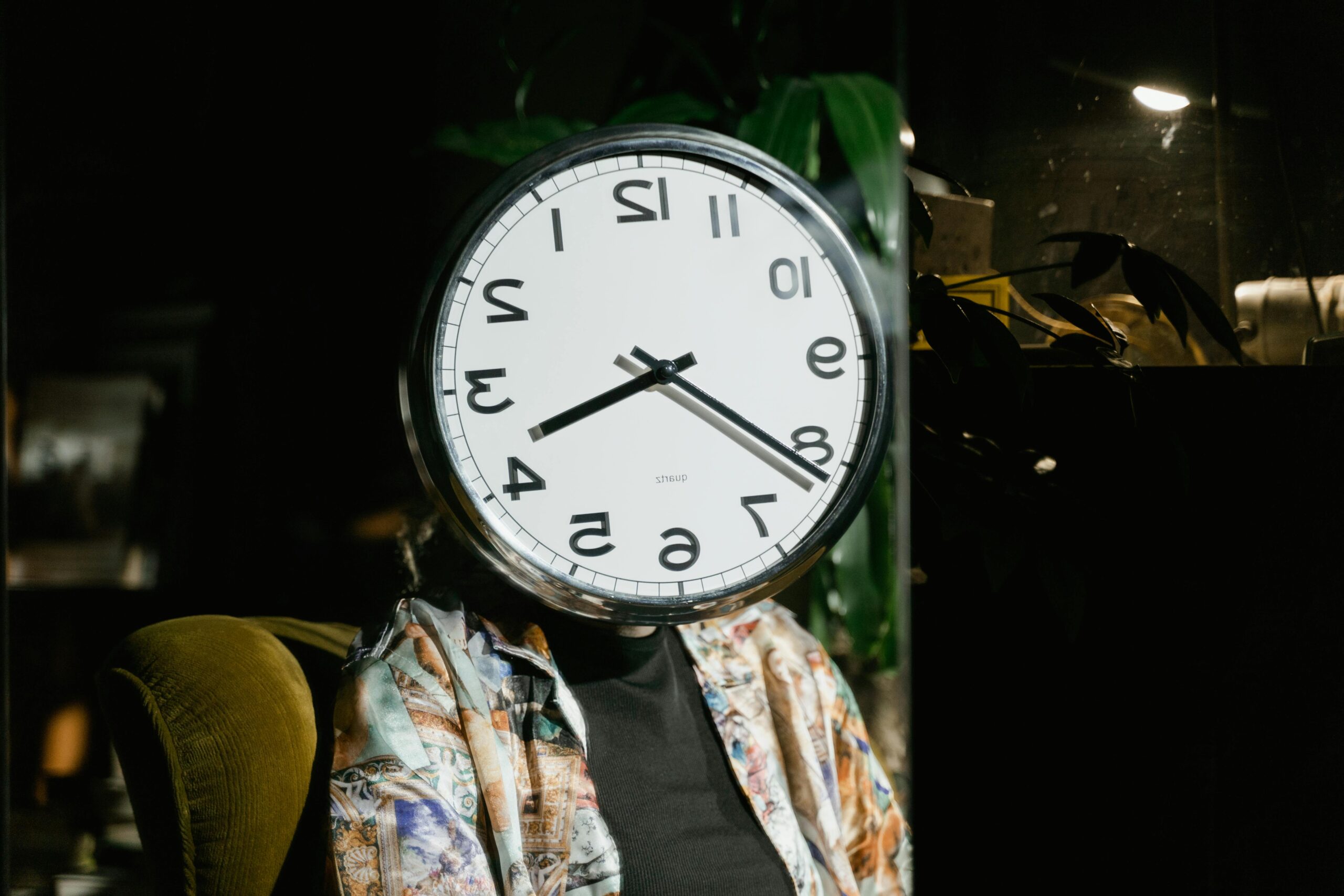 A person sits with a large wall clock covering their face, creating a surreal and artistic visual.