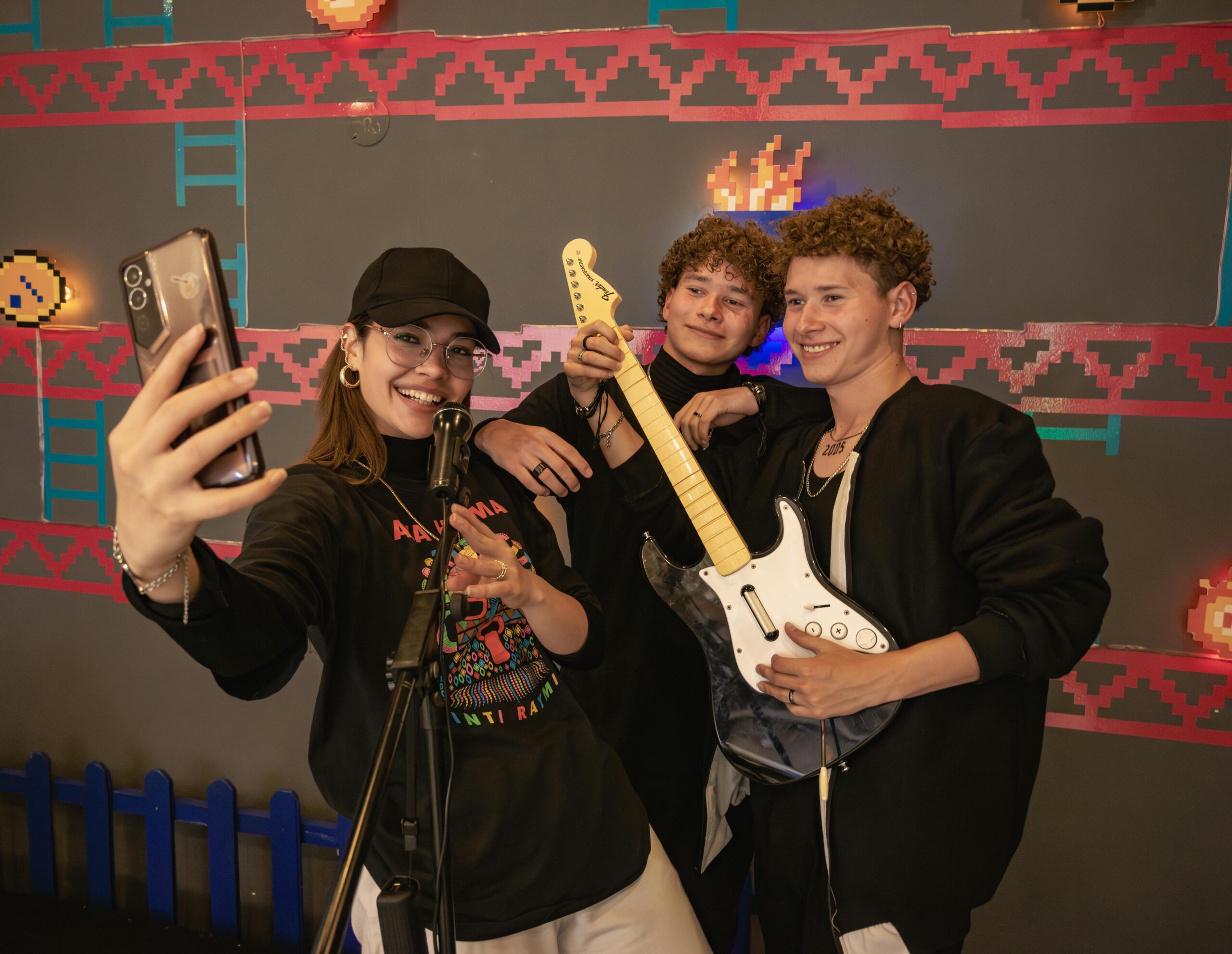 Teens capture a fun selfie with a guitar and microphone in front of a video game backdrop.