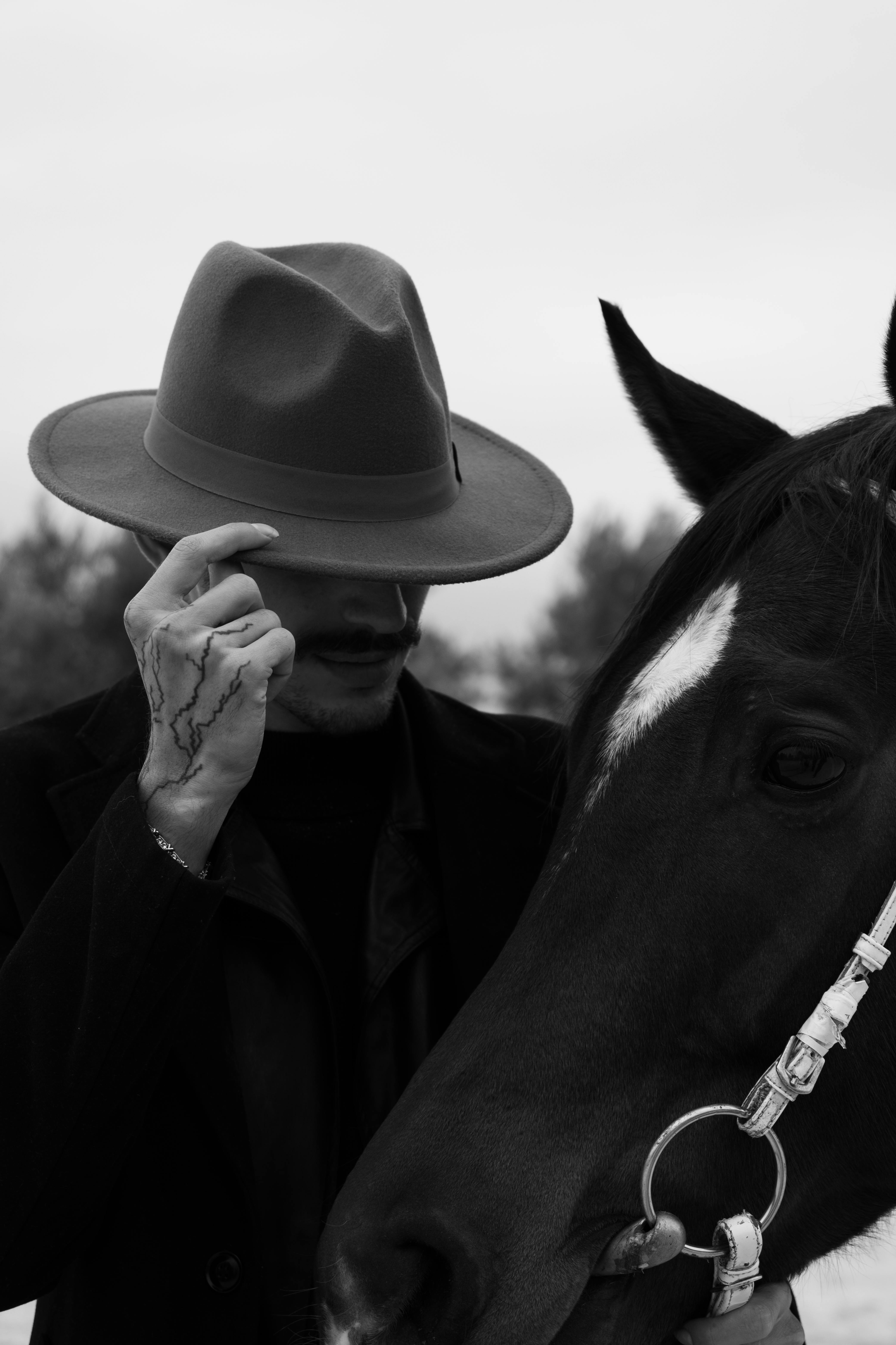 A man in a hat with a horse in a black and white photo, exuding a mysterious vibe.