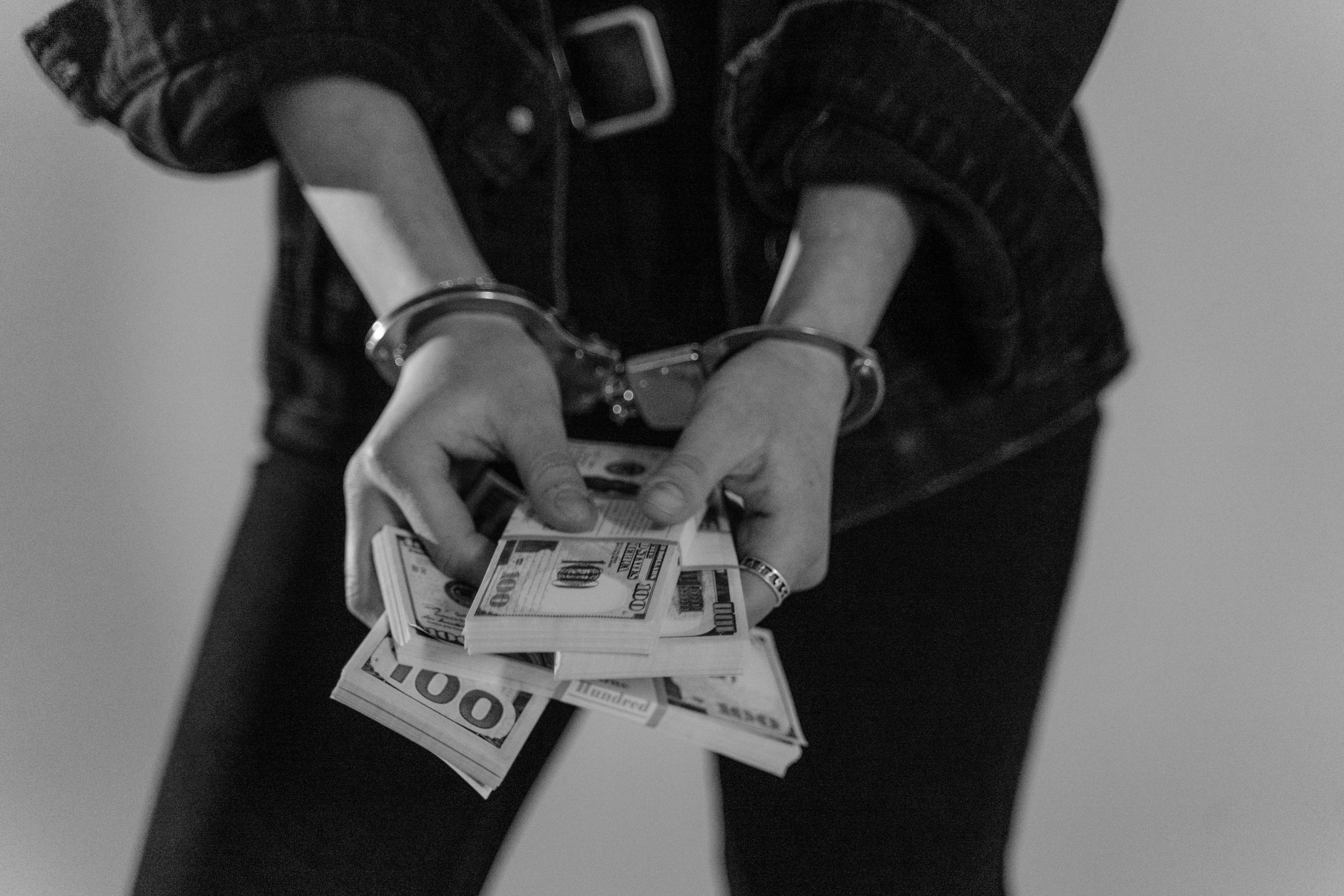 Black and white image of a handcuffed person holding bundles of US dollars.