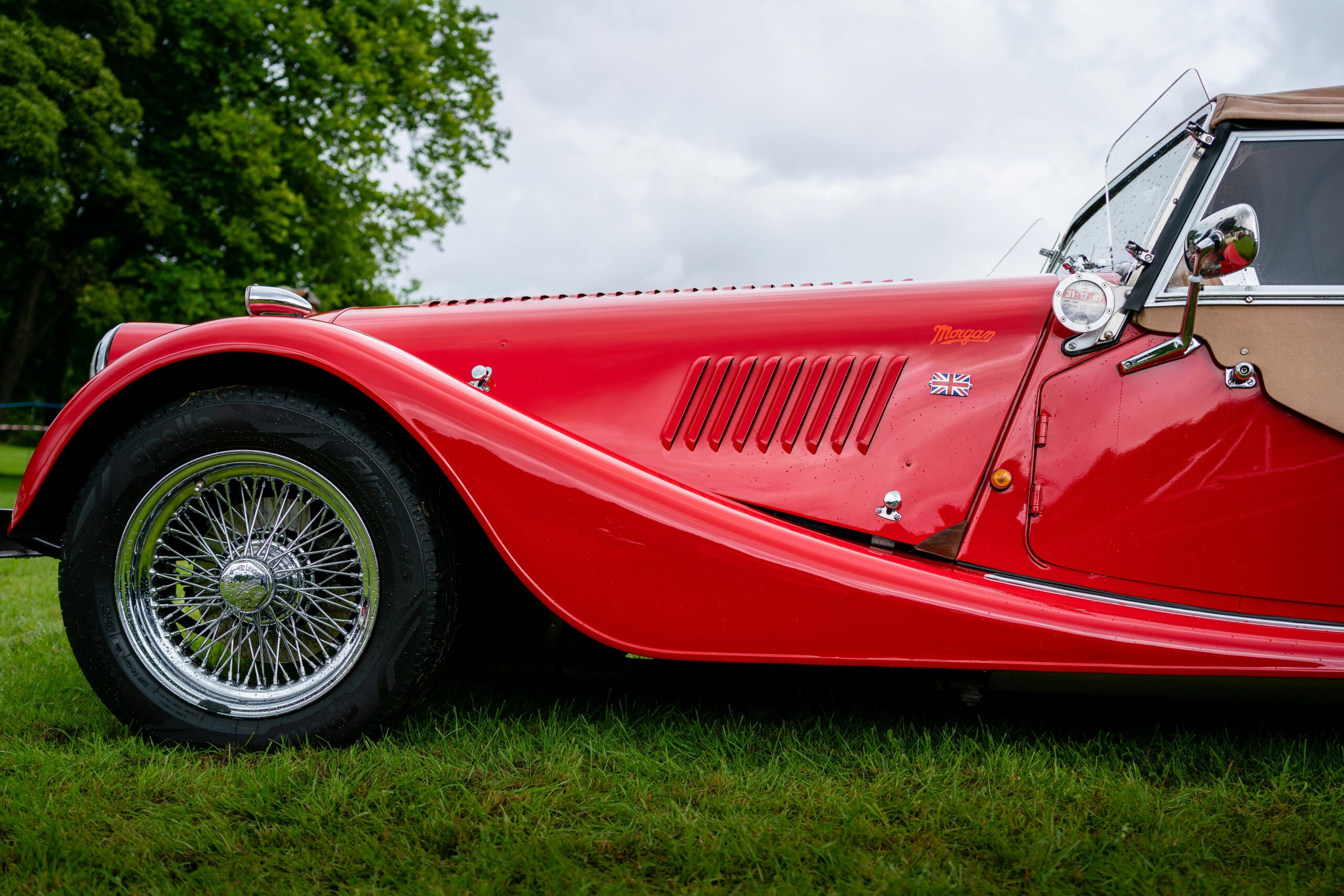 Capture of a vintage red Morgan car with British flag emblem, showcasing classic style.