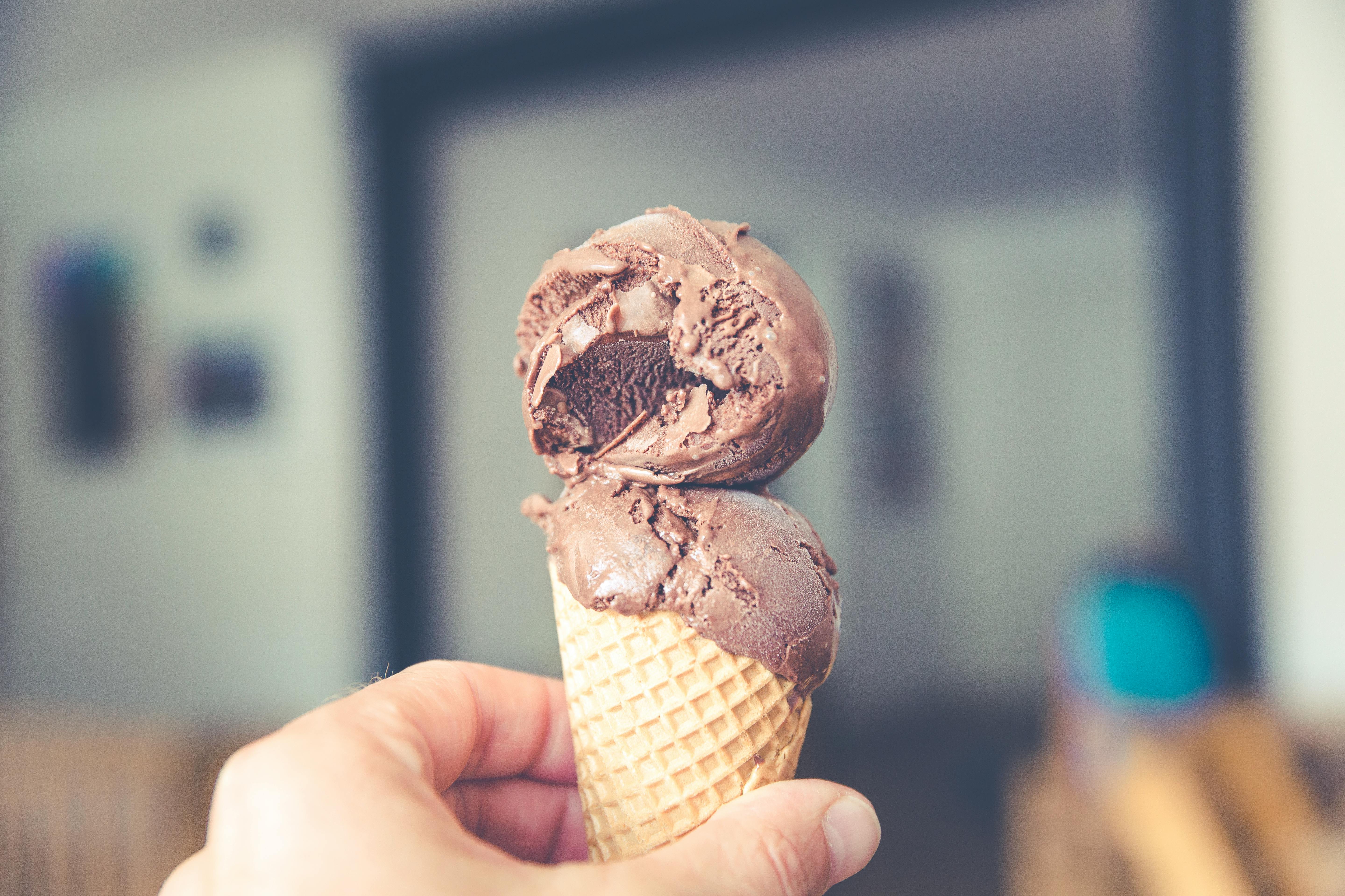 Close-up of a hand holding a chocolate ice cream cone indoors.