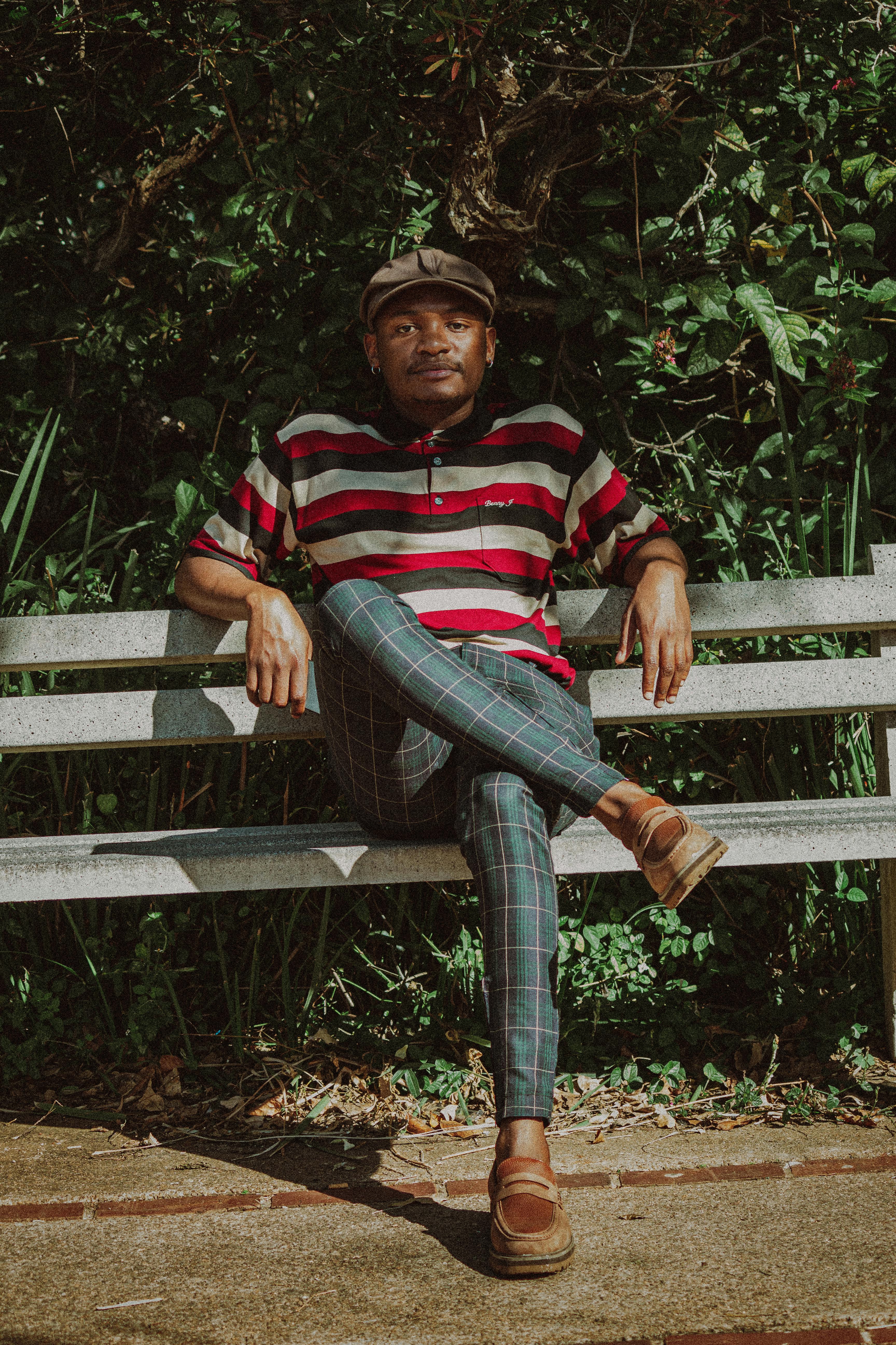 Fashionable man in striped shirt and cap relaxing on a bench in a sunny park.