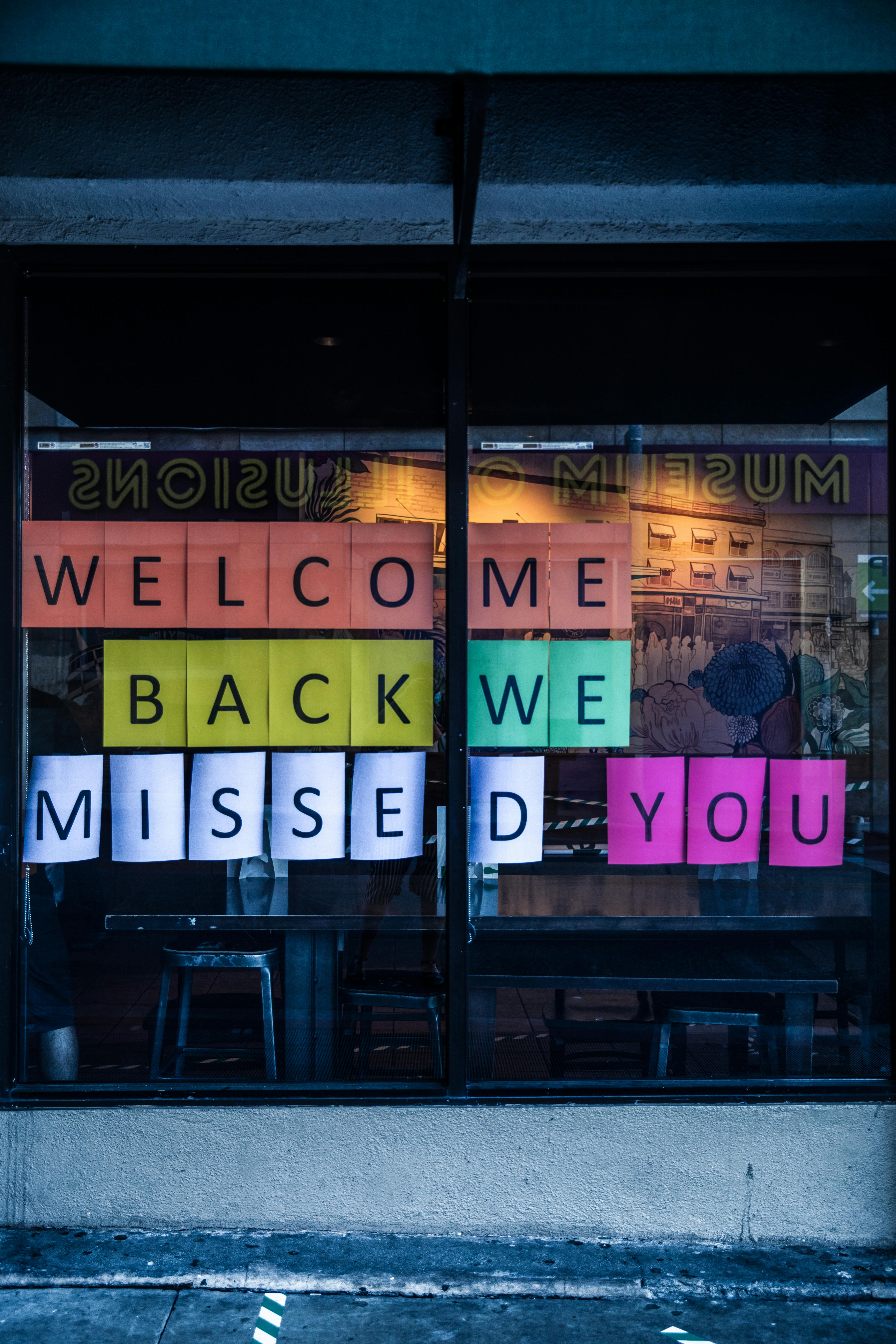 Vibrant welcome back sign displayed on a storefront window inviting customers to return.