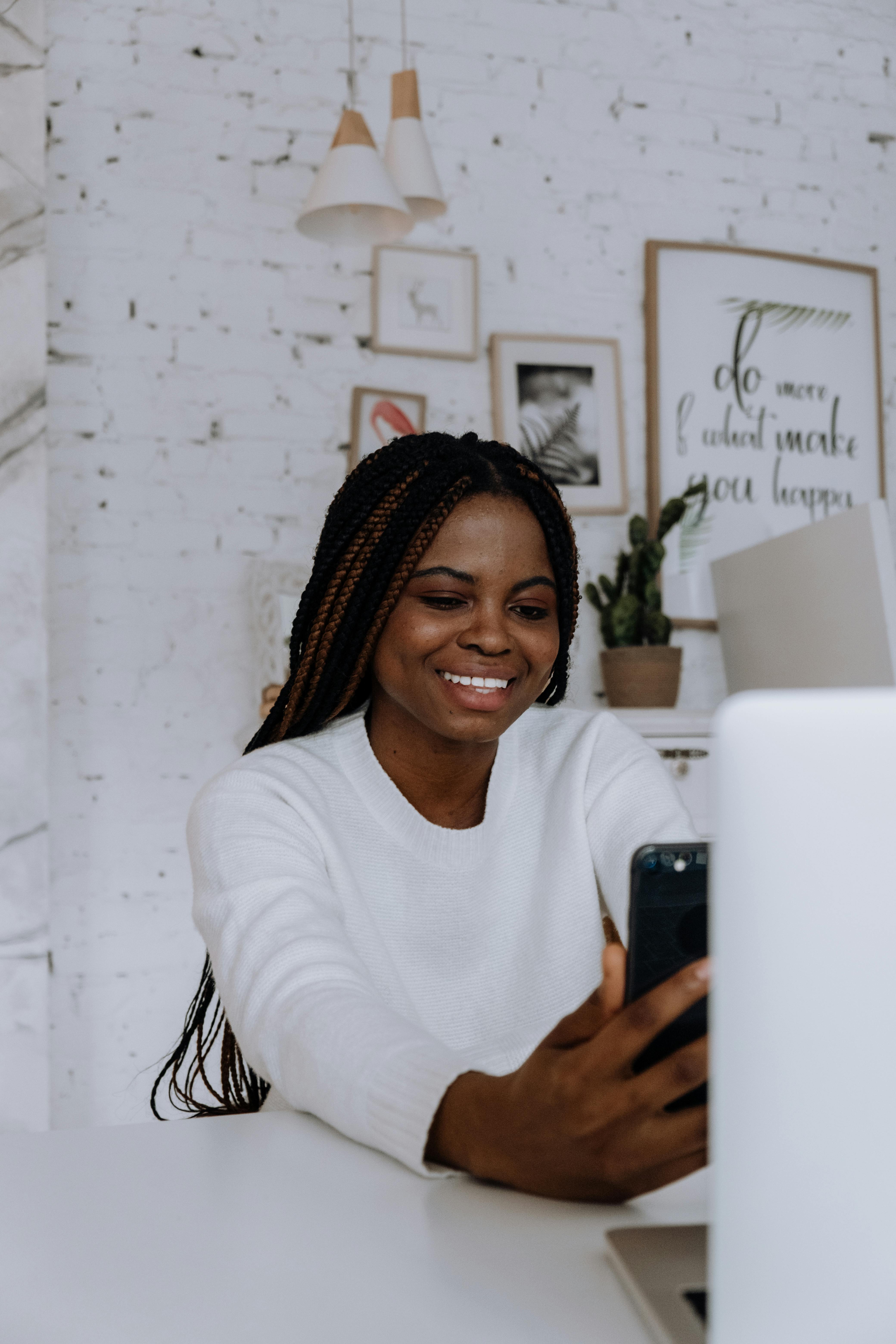 A smiling young woman with braids enjoying a video call in her minimalist apartment.