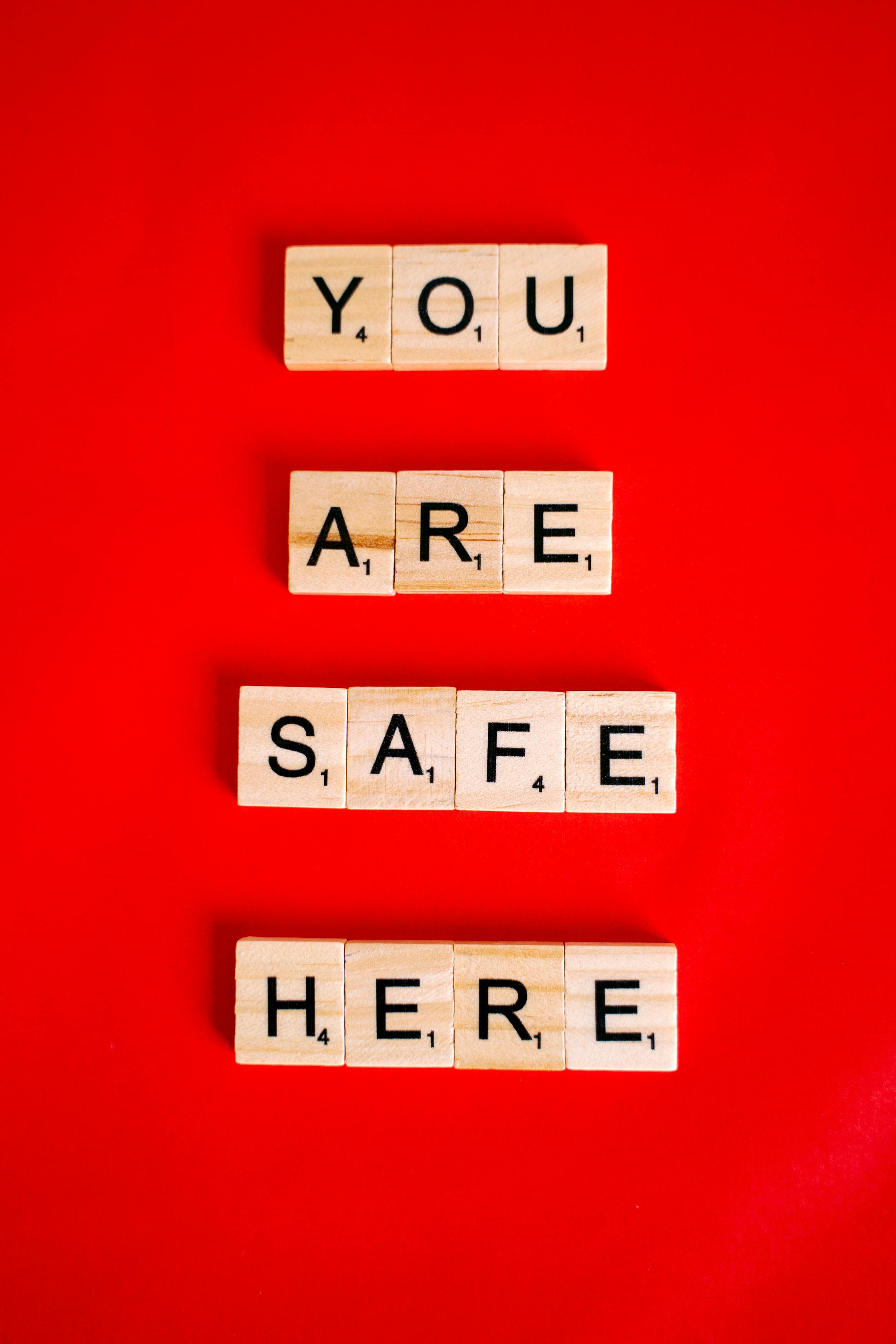 Wooden letter blocks spell 'You Are Safe Here' against a vibrant red background.