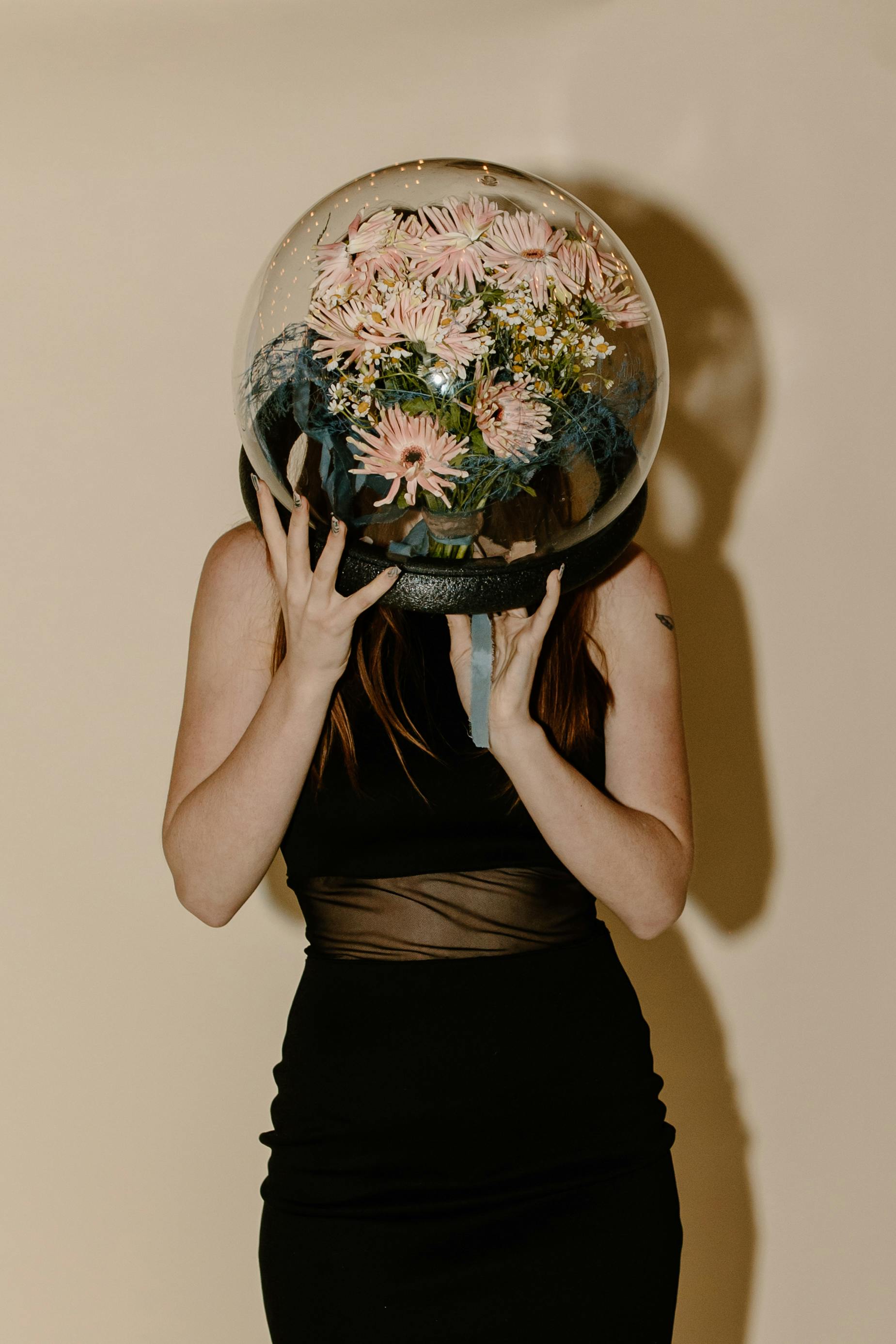 A creative portrait of a woman in a black dress wearing a floral-filled spacesuit helmet.